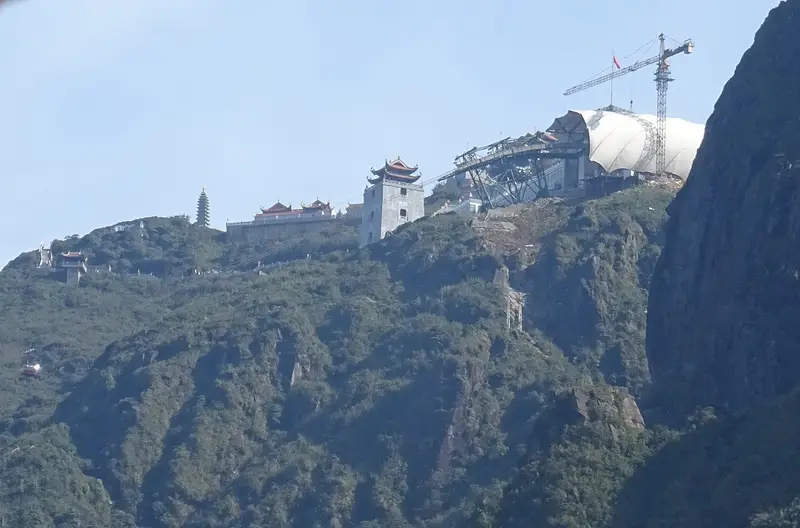 The cable car top station, a pagoda tower and temple buildings along the cliff edge below the Fansipan summit
